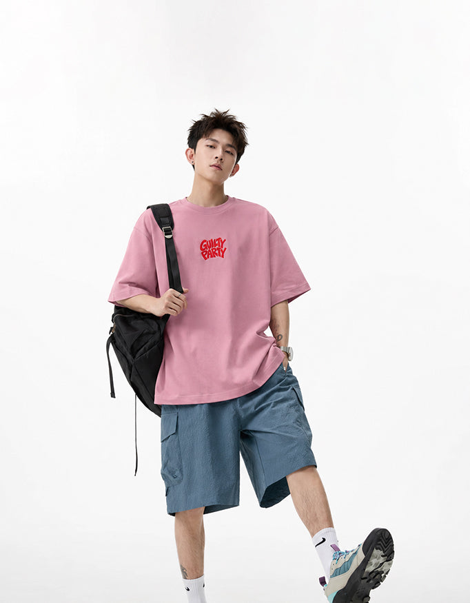 Male model wearing GUILTY PARTY pink oversized tee with red front chest logo in studio shoot