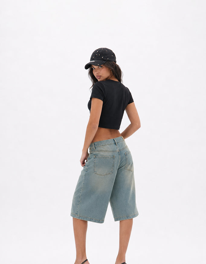 Back view of GUILTY PARTY black cropped baby tee styled with denim shorts in studio shoot