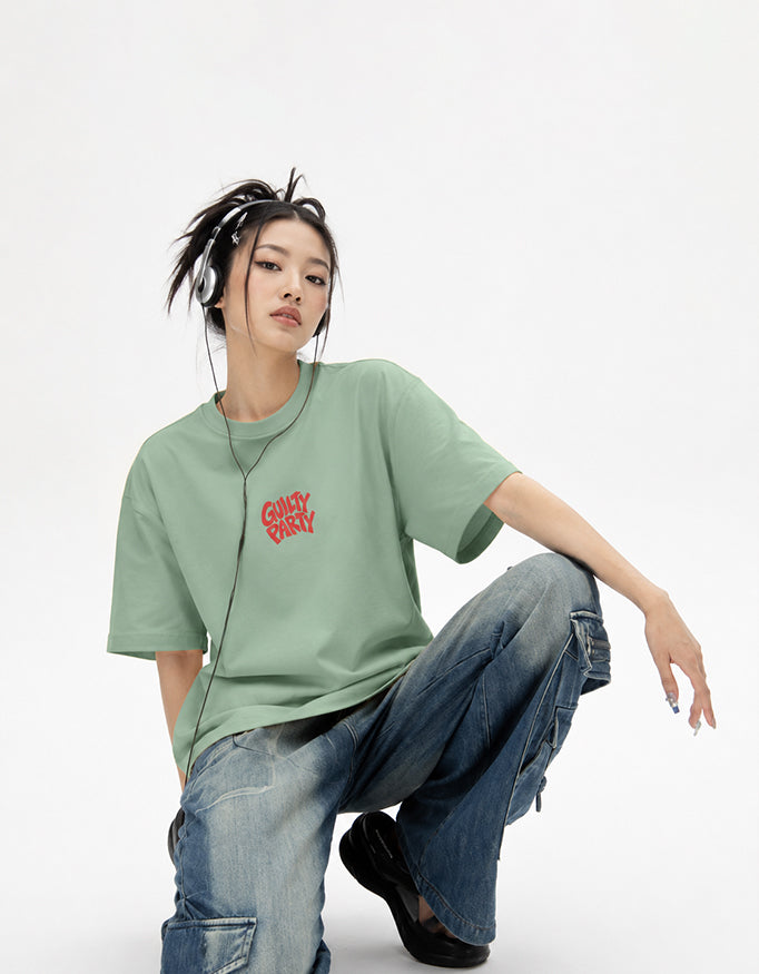 Female model wearing GUILTY PARTY Green oversized tee with red front chest logo in studio shoot