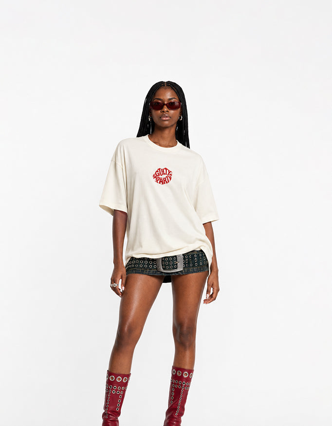 Male model wearing GUILTY PARTY off white oversized tee with small red front chest logo in studio shoot