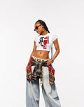Female model wearing GUILTY PARTY SPEAK white graphic baby tee with baggy jeans in a studio streetwear shoot